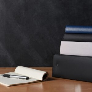 Teachers desk with note pad and pen and a stack of binders and books.