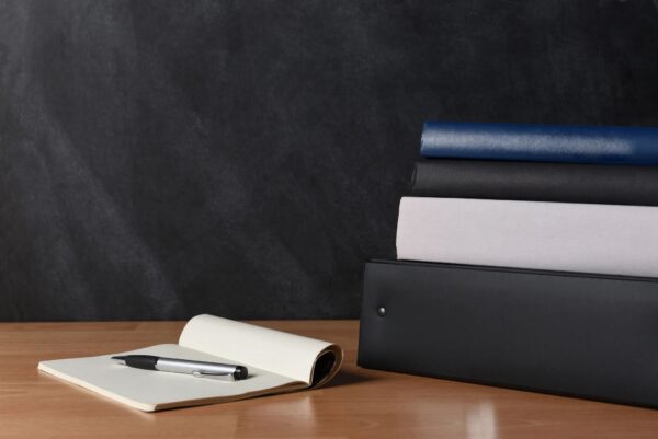 Teachers desk with note pad and pen and a stack of binders and books.